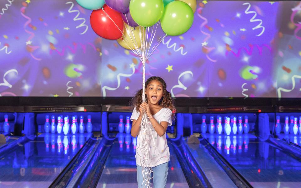 Girl with a balloon standing next to bowling lanes celebrating her birthday. 