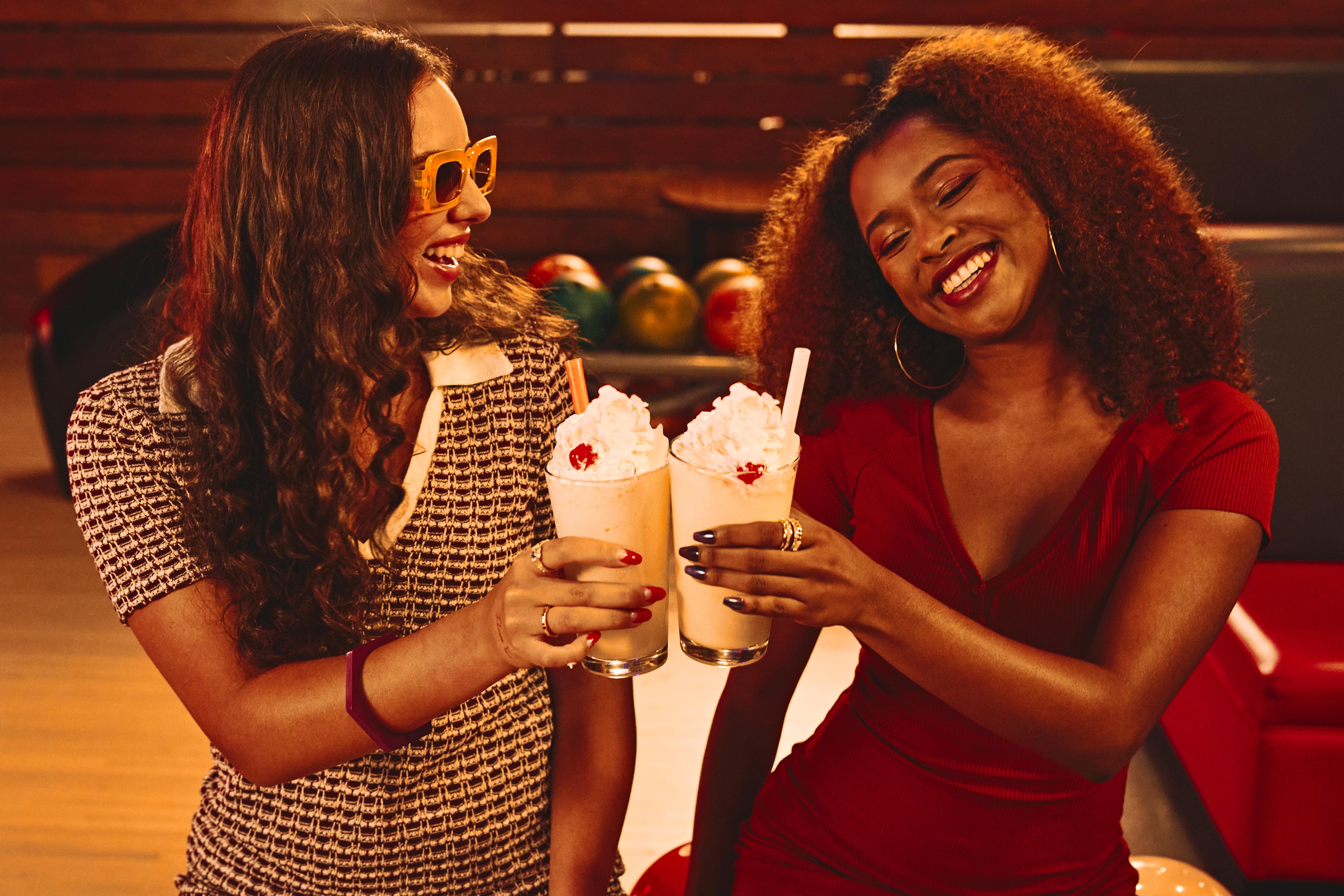 Two girls holding milkshakes on the lanes.