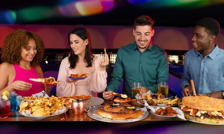 A group of friends enjoying food at the bowling alley with a variety of food. 