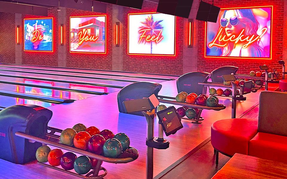 Bowling ball return with colorfully lit bowling lanes and neon signs in the background