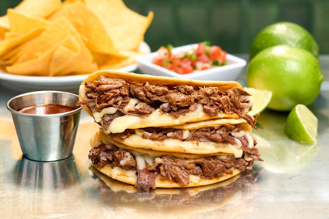 Birria street tacos stacked on top of one another with chips in the background. 