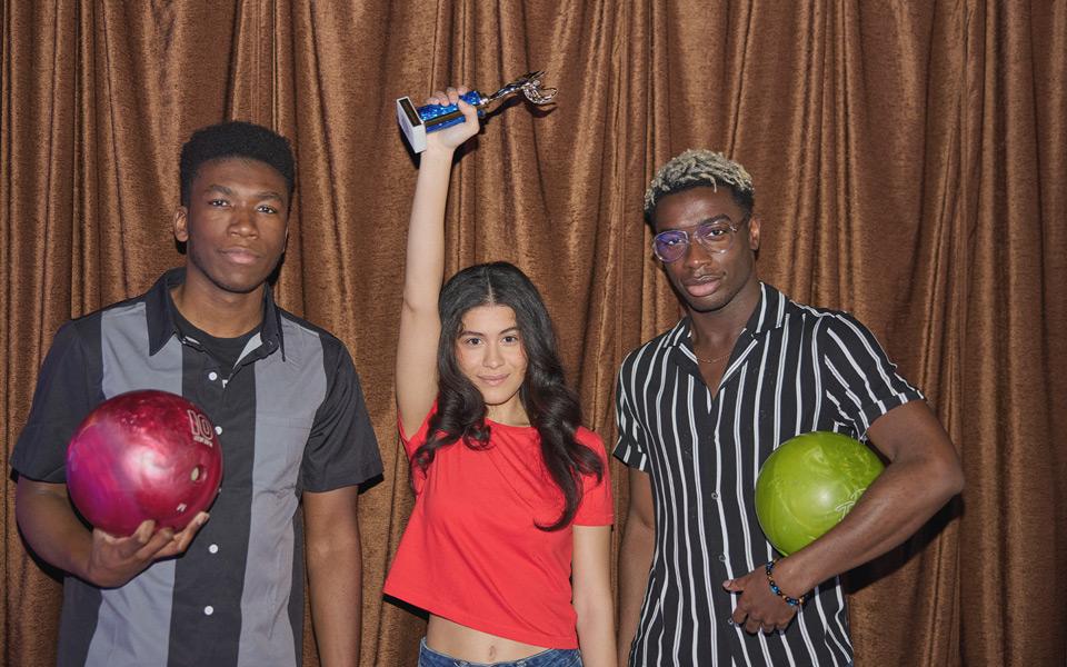 Three people holding up a trophy and bowling balls after winning a Bowling Tournament.