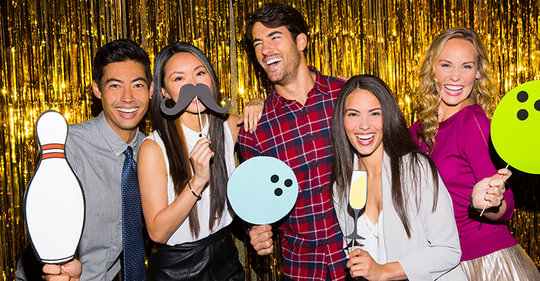 Friends posing in front of gold back drop with photo booth props